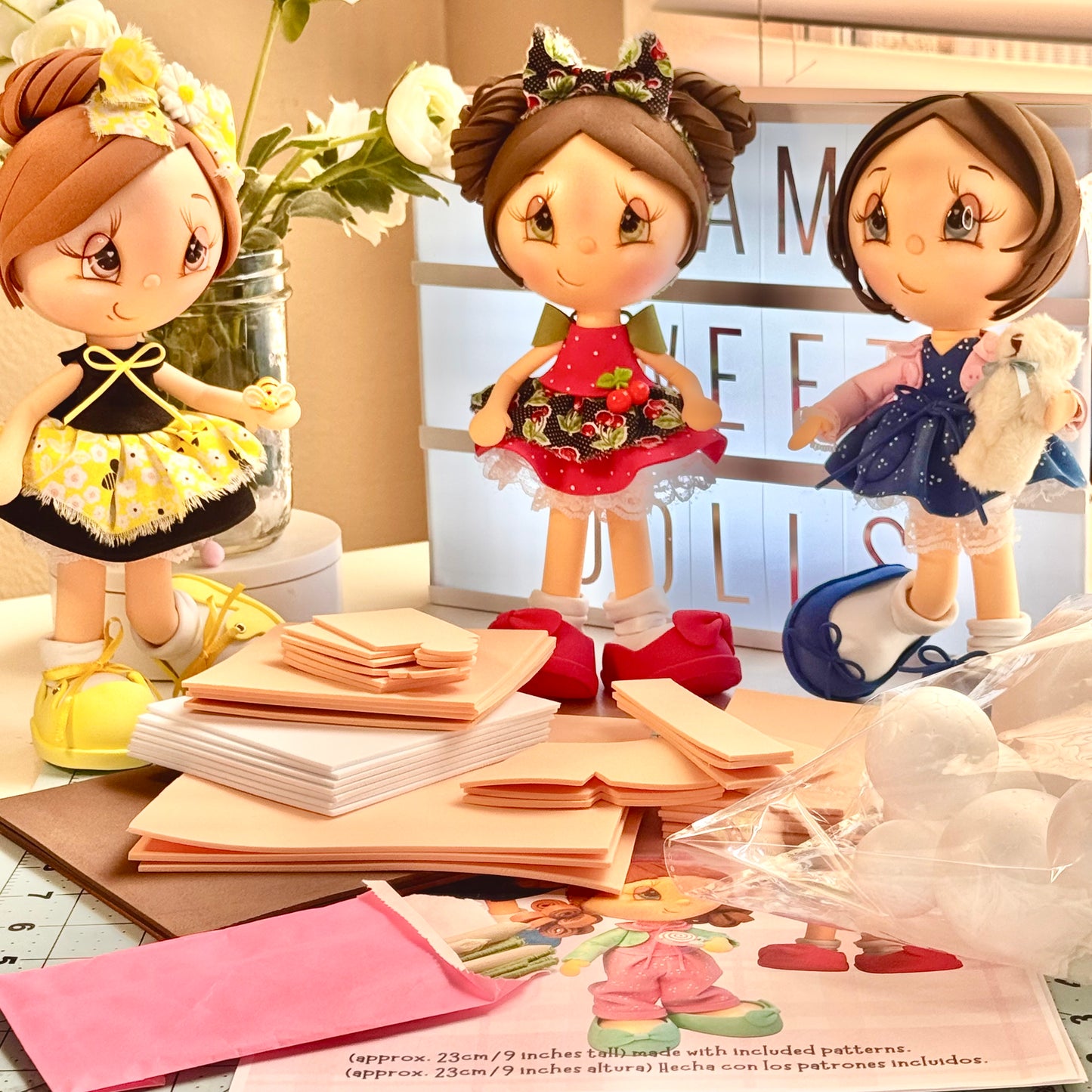 Materiales de foami precortado junto a tres muñecas fofuchas terminadas de 9 pulgadas - Pre-cut foam materials next to three finished 9-inch fofucha dolls.